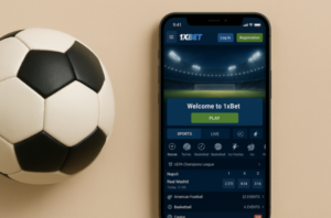 هاتف ذكي يعرض تطبيق 1xBet للمراهنات الرياضية، موضوع بجانب كرة قدم كلاسيكية بالأبيض والأسود على خلفية بلون بيج. تظهر على شاشة التطبيق واجهة ترحيبية ومباريات كرة قدم قيد المراهنة.